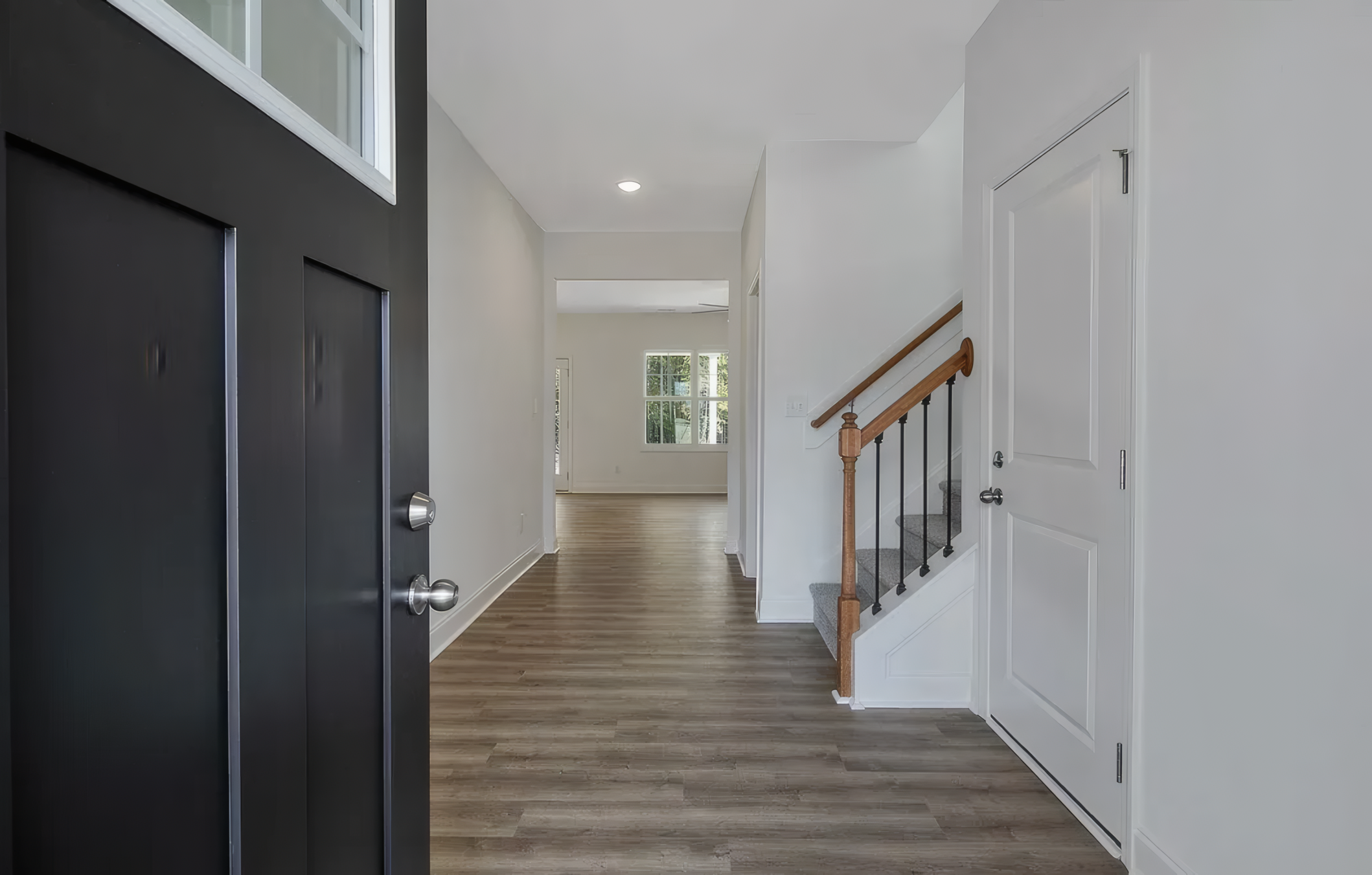 View of inside the house. You can see the black door from the entrance. In the distance is white walls and a staircase with a wood finish