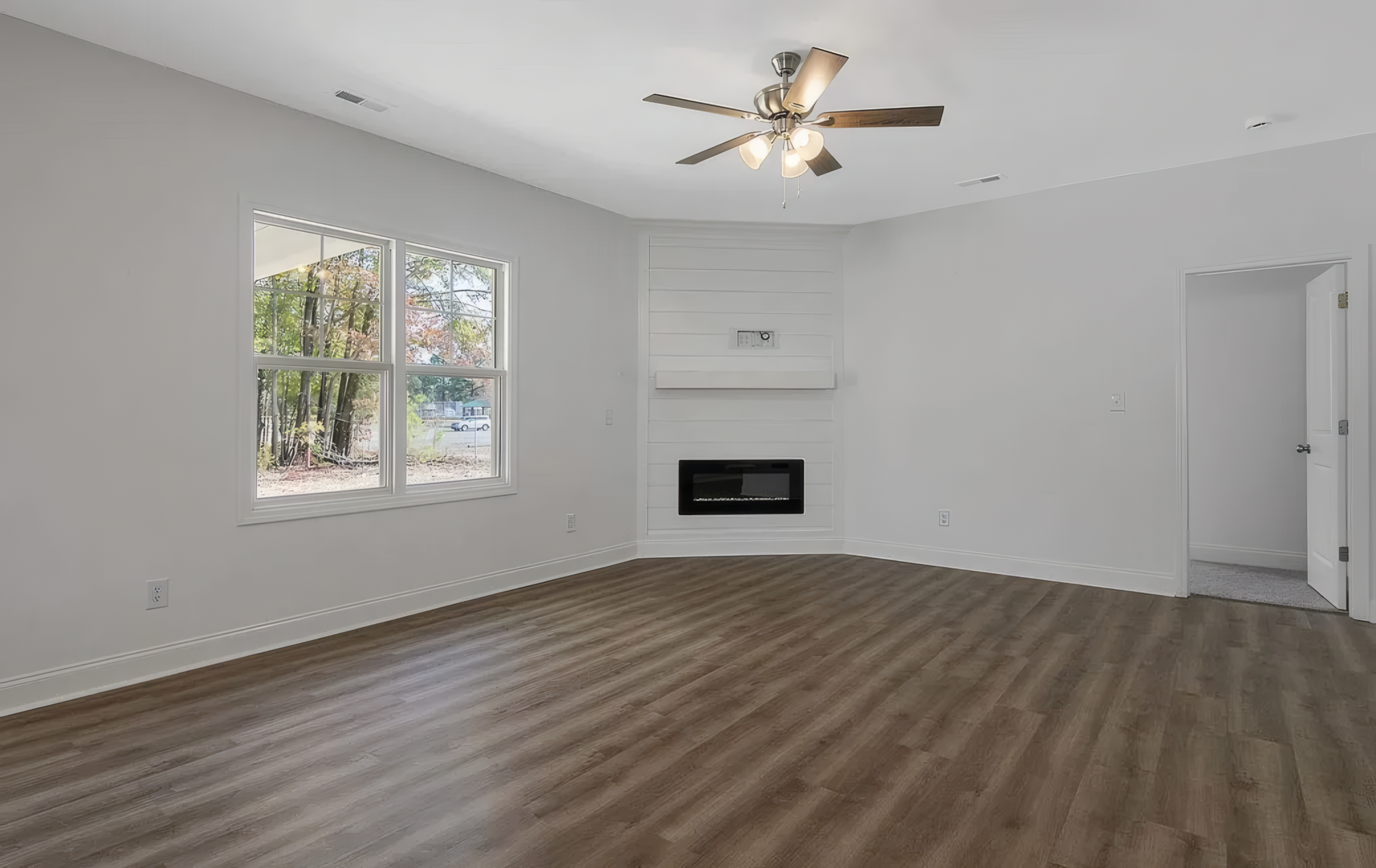 Empty room with a large window and ceiling fan. On the wall is a large build-in fireplace that has a small mantle above the fire section
