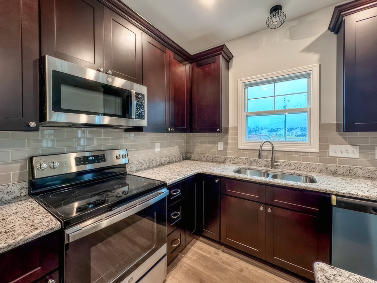 View of inside kitchen, there is a sink with a small window and a black oven that has a microwave above it