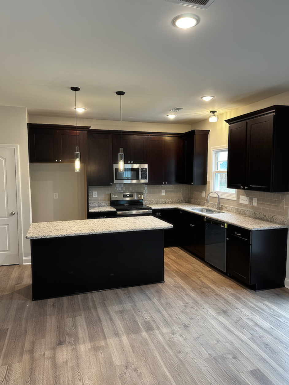 View of kitch from a distance, you can see the hanging lights and beautiful wooden flooring