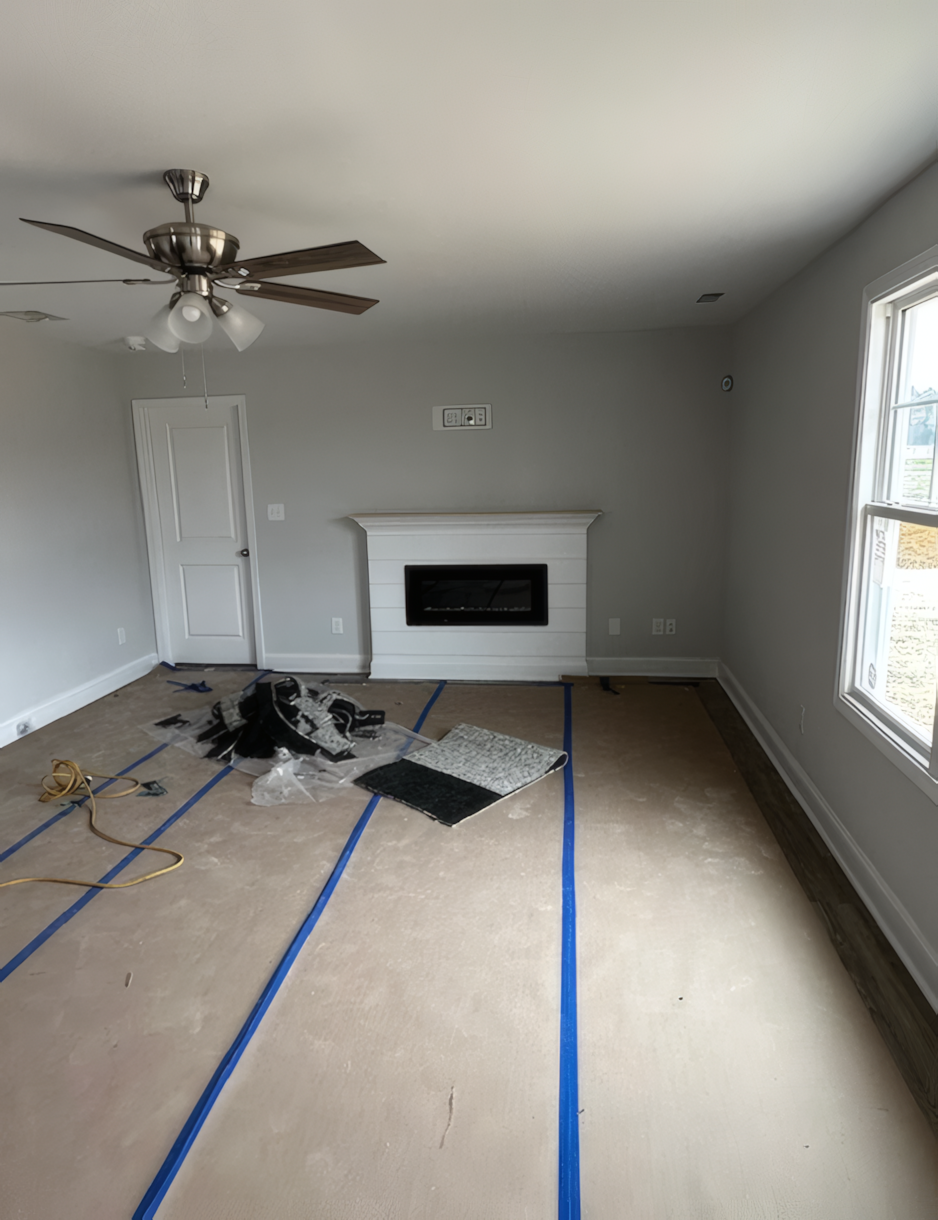 Large empty room with a small amount of construction paneling left on floor. There is a ceiling fan and a white build-in fireplace